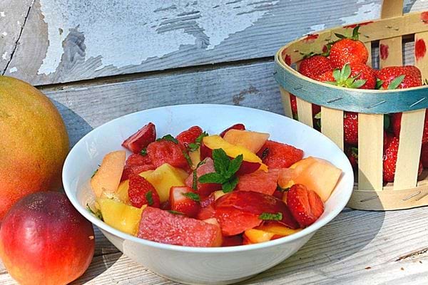 Une assiette blanche de salade de fruits d'été avec du melon avec un panier de fraises