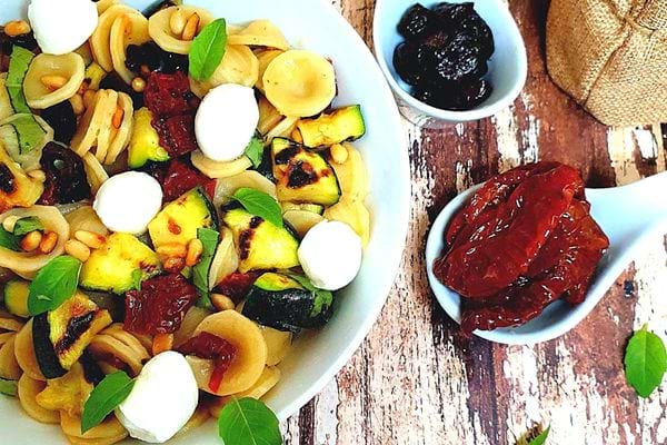 Une assiette de salade d'orecchiette aux tomates séchées, olives, courgettes grillées et pignons