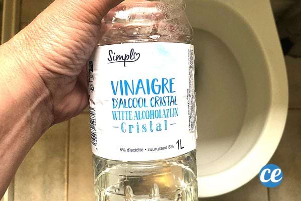 Une personne tenant une bouteille de vinaigre blanc au dessus des toilettes