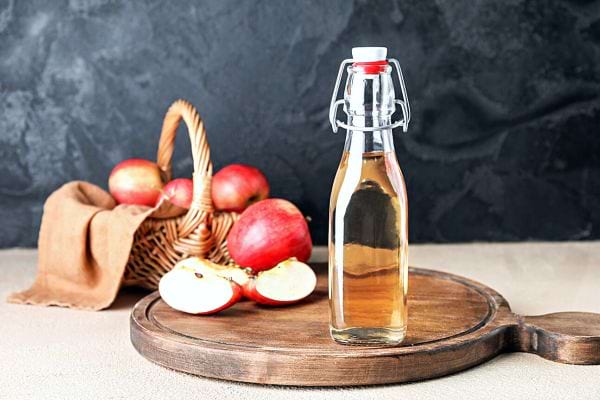 Une bouteille de vinaigre de cidre avec des pommes dans un panier 