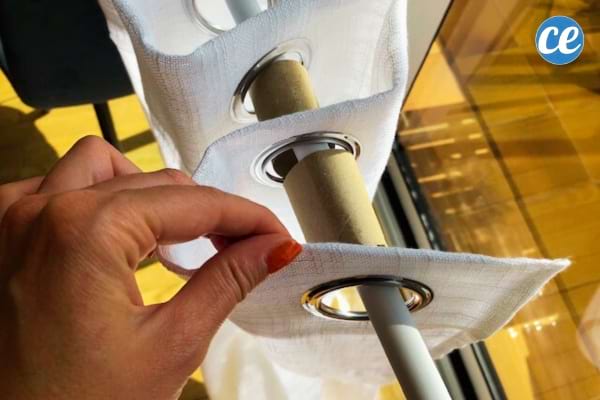 main qui tient un rideau blanc avec des rouleaux de papier toilettes entre les plis sur la tringle
