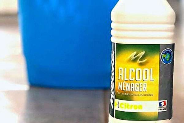 Une bouteille d'alcool ménager avec un seau bleu de serpillère en fond d'image 