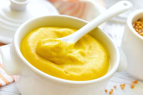 Une cuillère à café blanche dans un petit bol blanc de moutarde 