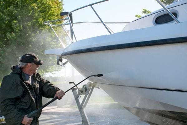 un homme nettoie la coque d'un bateau avec un karcher