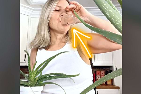 Une femme buvant dans un verre un bain de bouche avec du jus d’aloe vera avec des plantes sur les côtés 