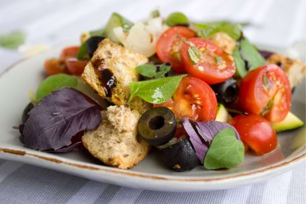 De la salade dans une assiette avec du pain, de la tomate et des olives