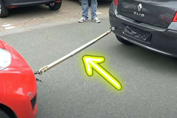 Une barre de remorquage qui lie une voiture rouge devant à une autre voiture grise foncée derrière