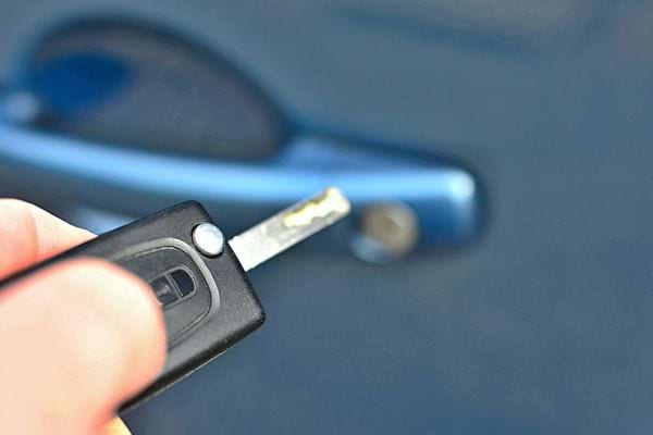 Une personne ayant une clé de sa voiture dans sa main devant sa voiture bleue