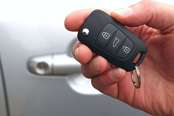 Une personne tenant une clé de voiture devant sa porte de voiture grise 