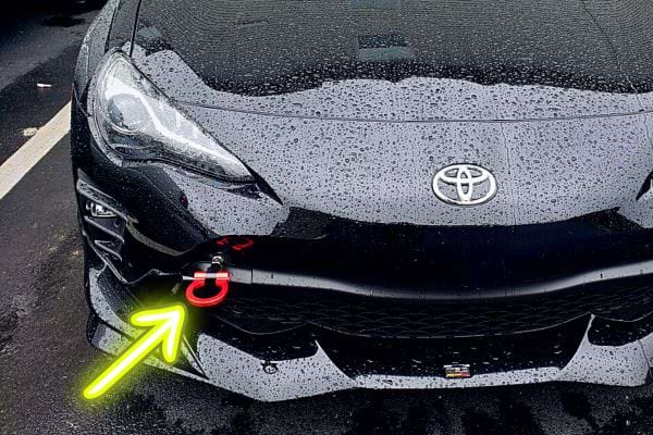Une flèche jaune fluo sur un crochet de remorquage rouge d'une voiture Toyota noir