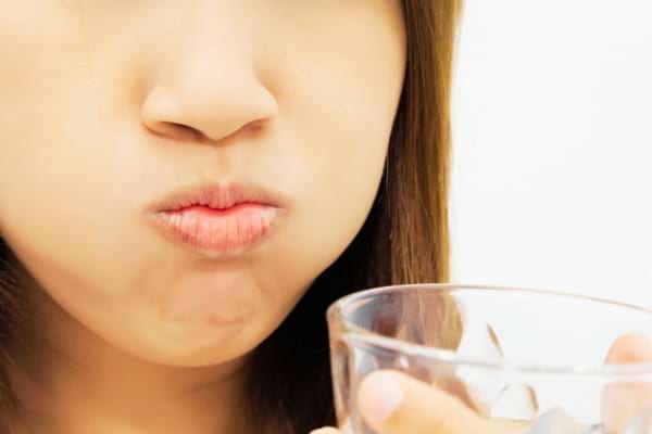 Une femme qui se gargarise à l'eau salée pour soigner sa langue fissurée