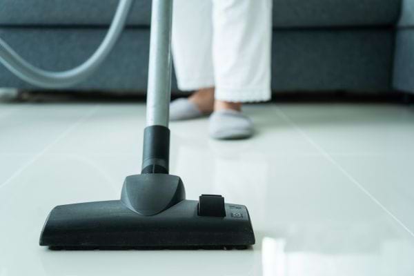 une femme passe l'aspirateur sur le carrelage blanc