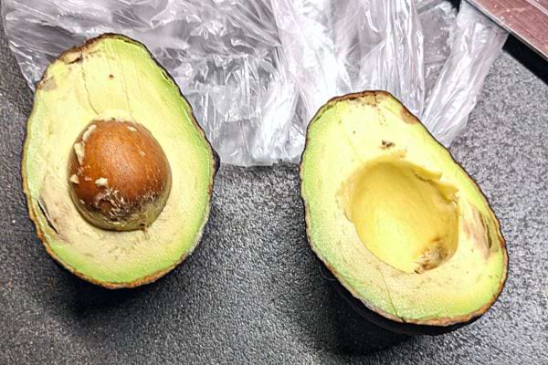 Un avocat ouvert en deux avec son noyau proche d'un sachet en plastique