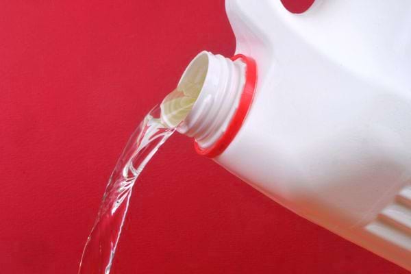Un liquide transparent sortant d'une bouteille blanche sur un fond rouge 