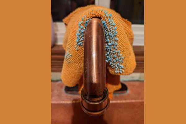 Un chiffon micro-fibre orange avec un produit bleu dessus posé sur du cuivre