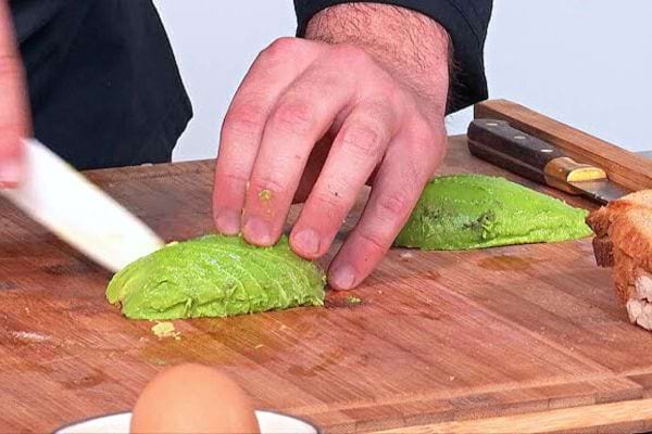 Un cuisiner avec un tablier noir coupant un avocat