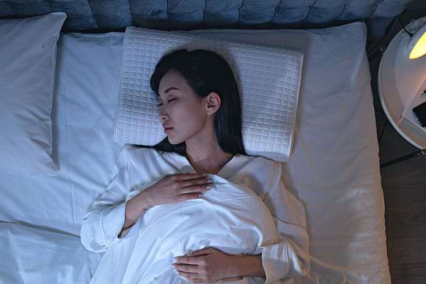 Une femme asiatique qui dort sur le dos dans un lit avec la tête sur le côté