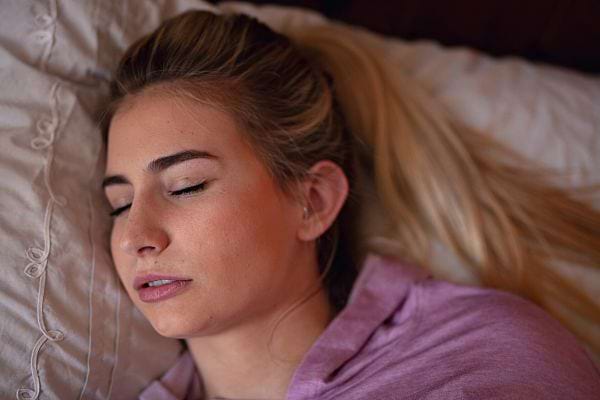 Une femme blonde habillée d'un haut violet qui a l'air de dormir sur le côté 