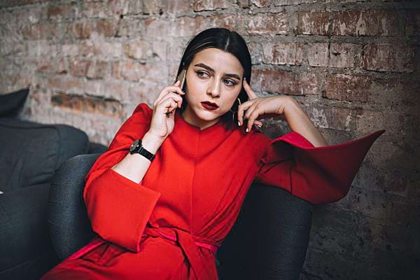 Une femme assise sur un canapé vêtu d'une robe rouge qui est au téléphone avec un air fâché