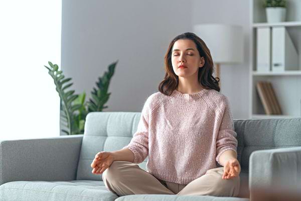 Une femme en train de méditer sur son canapé 