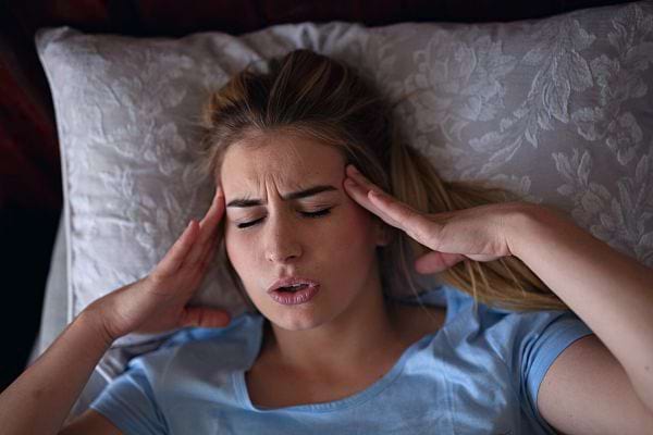 Une femme couchée sur son oreiller se tenant la tête 
