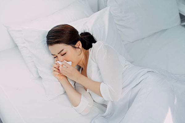 Une femme habillée en blanc dans un lit blanc qui se mouche 
