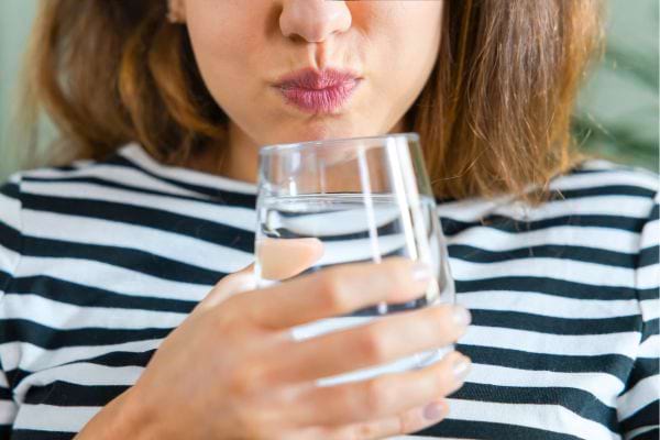 Une femme qui tient un verre pour faire une gargarisation d’eau salée contre la toux.