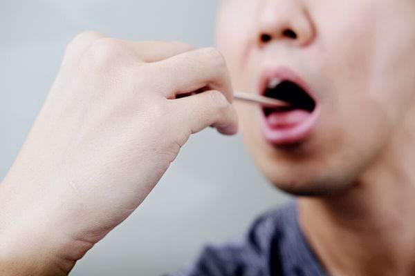 Un homme se faisant consulter l'intérieur de la bouche à l'aide d'un bâton 