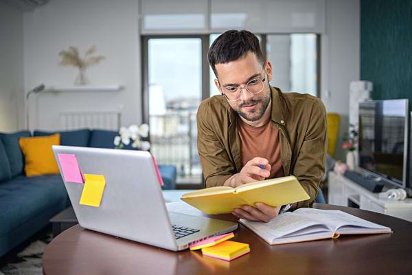 Un homme tenant un livre proche d'un ordinateur 
