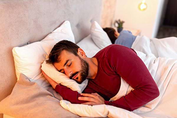Un homme couché sur le côté dans un lit avec une femme de l'autre dans la même position 