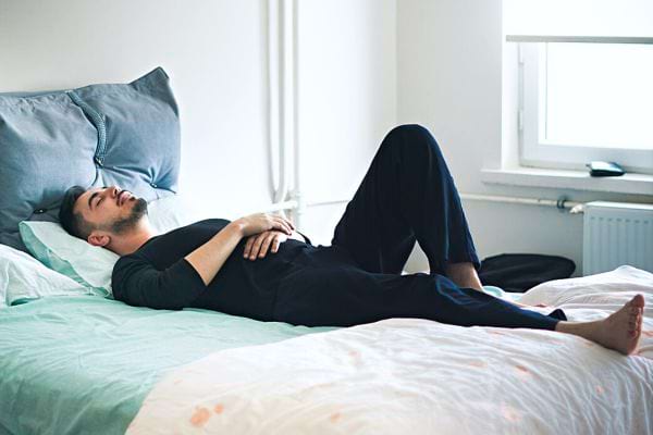 Un homme couché sur le dos dans un lit avec sa jambe gauche relevée