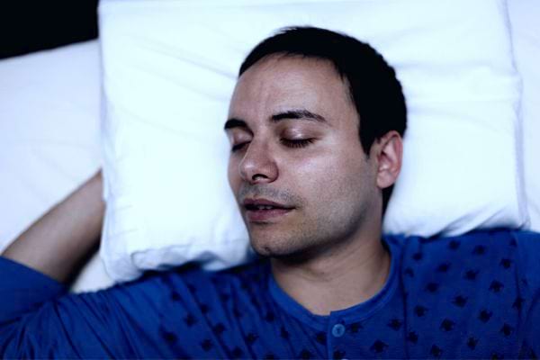 Un homme qui dort dans un lit sur un oreiller blanc habillé d'un haut bleu 