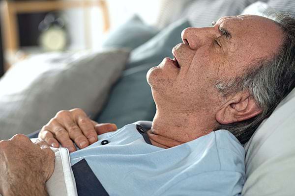Un homme âgé qui dort sur le dos avec la bouche ouverte avec un air de soufrrance 