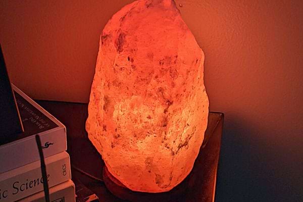 Une lampe de sel allumée dans le noir proche de plusieurs livres