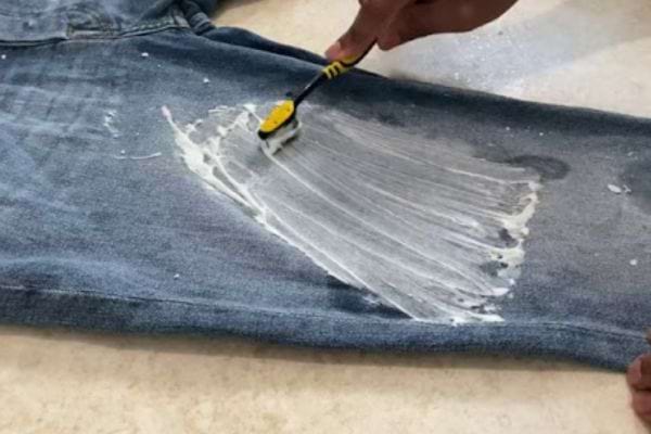 Eine Person reinigt mit einer gelben Zahnbürste einen Farbfleck von Blue Jeans