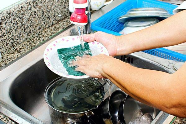Personne faisant la vaisselle avec une éponge verte et un robinet rouge 
