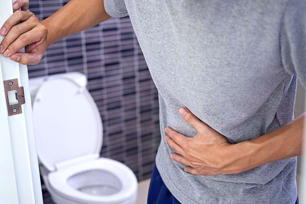 Une personne tenant le mur et son ventre en sortant des toilettes avec un tee-shirt gris 