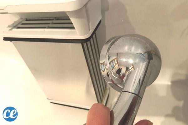 Une personne tenant un pommeau de douche devant un condenseur 