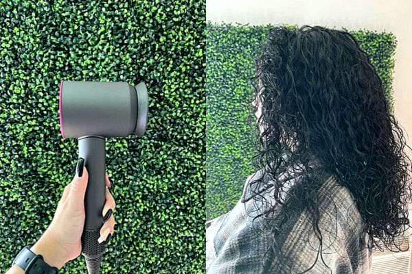 Une femme ayant du vernis noir sur les ongles tenant un sèche-cheveux avec des cheveux noirs