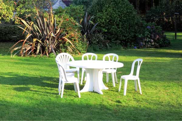 Un grand jardin avec une table blanche et des chaises blanches de pique-nique tout autour