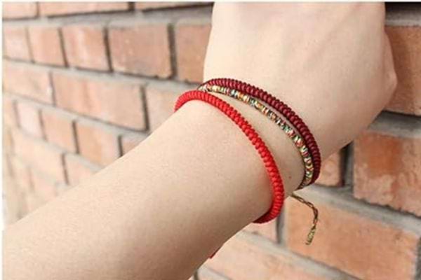 Une personne touchant un mur de brique ayant trois bracelets rouges à son poignet