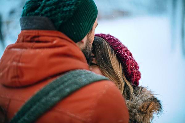 Un homme avec un bonnet vert faisant un bisous sur le front d'une femme dans la neige