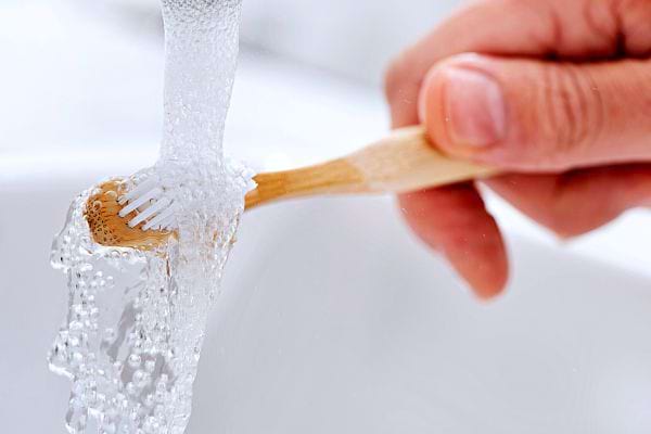 Une personne mettant une brosse à dents en bois sous de l'eau