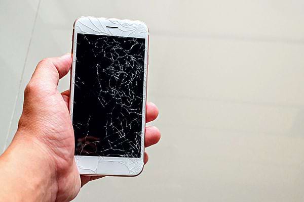 Une personne tenant un téléphone avec l'écran fissuré 