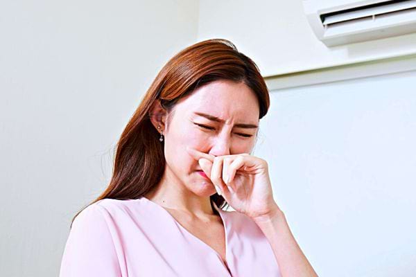 Une femme asiatique vêtu d'un haut rose qui fait une grimace et qui bouche son nez