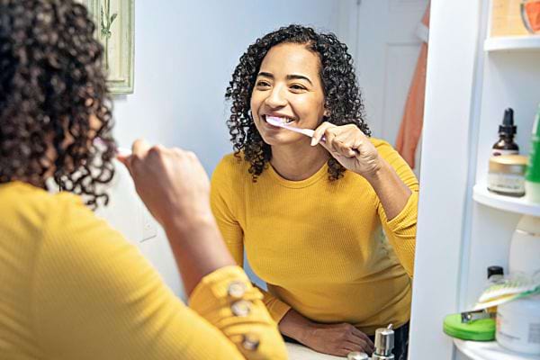 Une femme avec un haut jaune qui se brosse les dents devant son miroir 