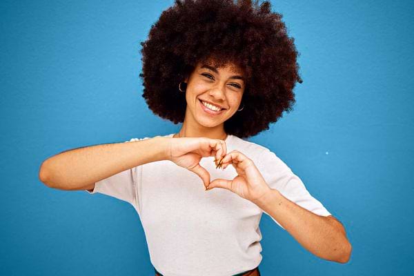 Une jeune femme avec un afro faisant un coeur avec ses mains 