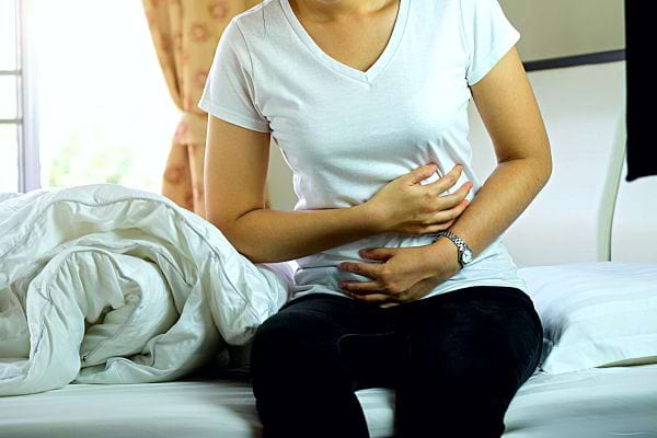 Une femme assise sur son lit se tenant le ventre