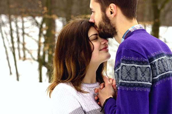 Un homme faisant un bisous sur le front d'une femme dans la neige