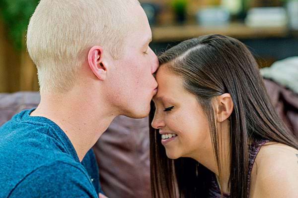Un homme blond faisant un bisous sur le front d'une femme